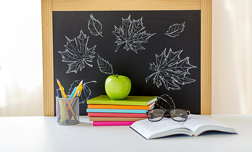 education and learning concept - books, apple, chalkboard and school supplies on table at home