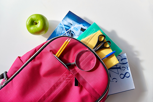 education and learning concept - pink backpack with books and school supplies, green apple on table