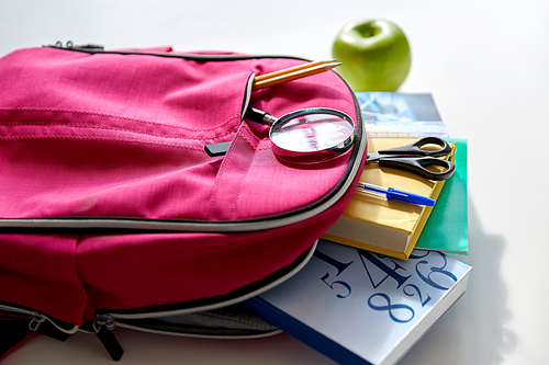 education and learning concept - pink backpack with books and school supplies, green apple on table