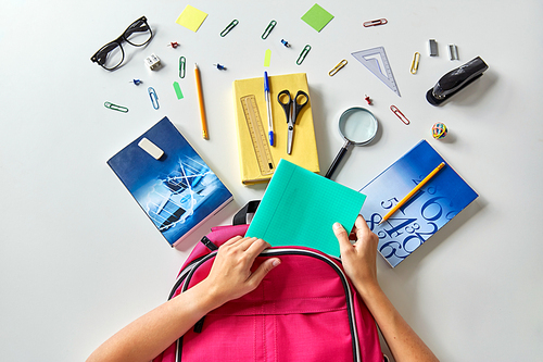 education and learning concept - hands packing pink backpack with books and school supplies on table