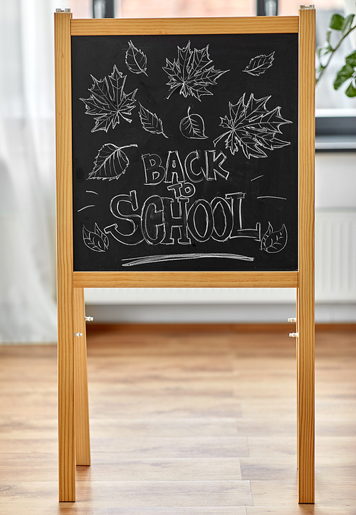 education and learning concept - autumn leaves and back to school words drawn with chalk on chalkboard at home