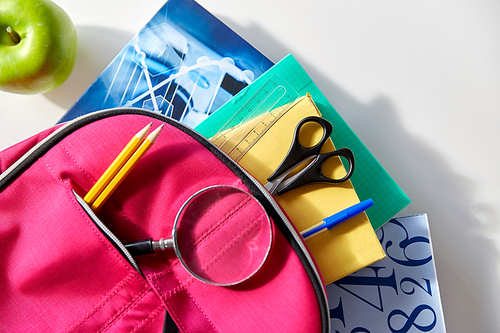 education and learning concept - pink backpack with books and school supplies, green apple on table