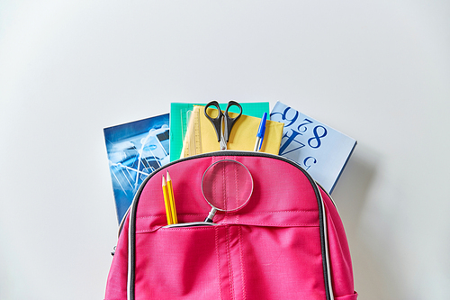 education and learning concept - pink backpack with books and school supplies on table