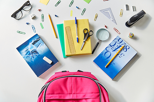 education and learning concept - pink backpack with books and school supplies on table