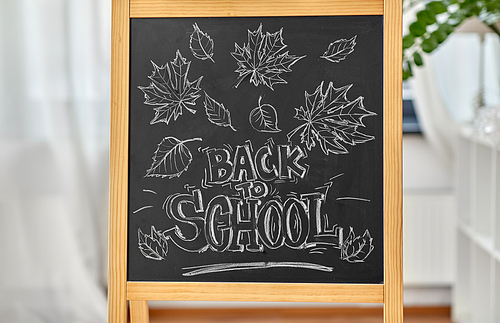 education and learning concept - autumn leaves and back to school words drawn with chalk on chalkboard at home