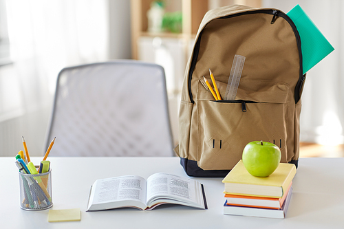 education and learning concept - books, apple and school supplies on table at home