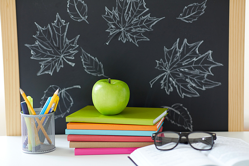 education and learning concept - books, apple, chalkboard and school supplies on table at home