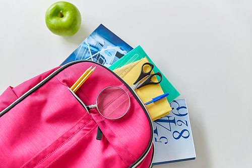 education and learning concept - pink backpack with books and school supplies, green apple on table