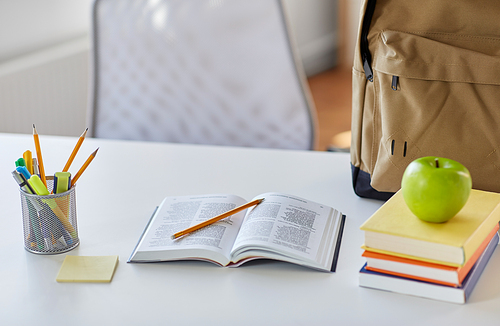 education and learning concept - close up of books, apple and school supplies on table at home