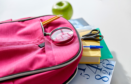 education and learning concept - pink backpack with books and school supplies, green apple on table