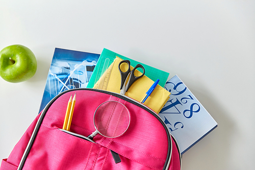 education and learning concept - pink backpack with books and school supplies, green apple on table