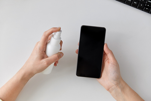 hygiene, cleaning and disinfection concept - close up of woman hands spraying hand sanitizer to smartphone