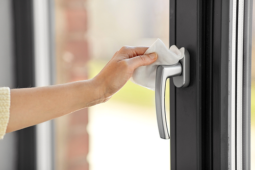 hygiene, health care and safety concept - close up of woman hand cleaning window handle surface with wet wipe