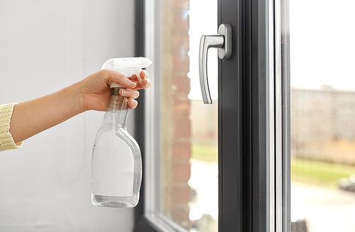 hygiene, health care and safety concept - close up of female hands cleaning window handle surface with detergent spray