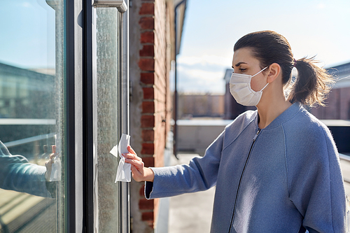 hygiene, health care and safety concept - woman in face protective medical mask cleaning door handle with antiseptic wet wipe