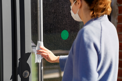 hygiene, health care and safety concept - close up of woman in mask cleaning outdoor door handle with antiseptic wet wipe