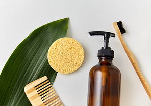 natural cosmetics, sustainability and eco living concept - wooden comb, sponge, liquid soap or shower gel and green leaf on white background