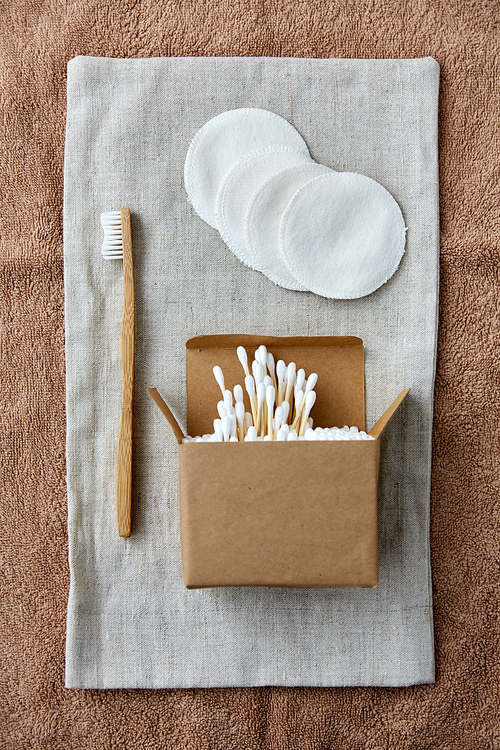 natural cosmetics, sustainability and eco living concept - wooden toothbrush, cotton pads and swabs in paper box on canvas bag and bath towel
