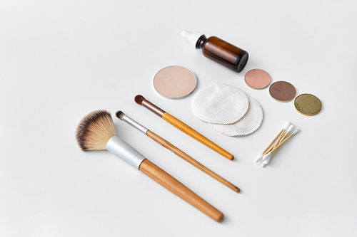 natural cosmetics and eco living concept - wooden make up brushes, cotton pads and swabs, eye shadows and essential oil or serum on white background