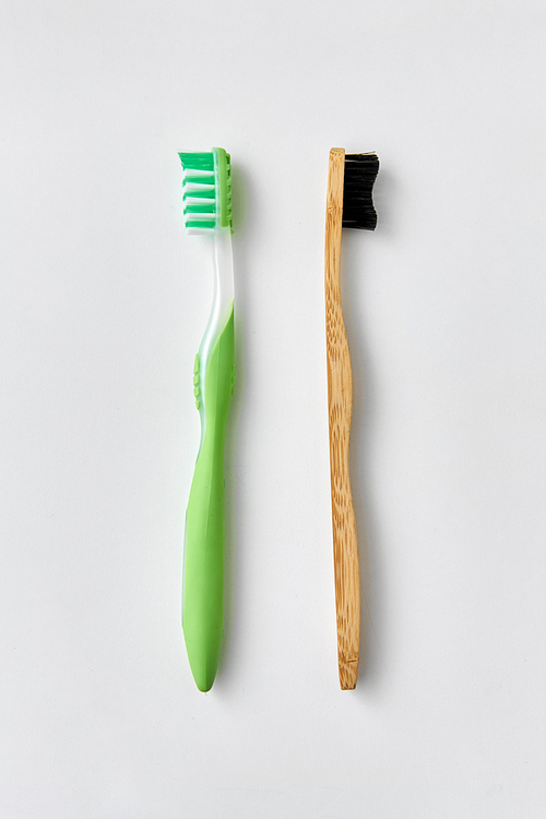 dental care, sustainability and eco living concept - wooden and plastic toothbrush on white background