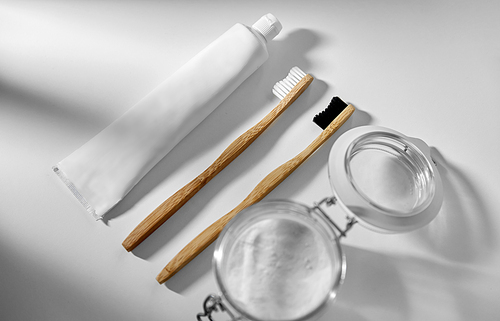 dental care, sustainability and eco living concept - wooden toothbrushes, toothpaste and washing soda in glass jar on white background