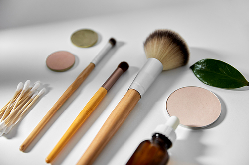 natural cosmetics and eco living concept - wooden make up brushes, cotton pads and swabs, eye shadows and essential oil or serum on white background