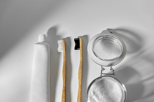 dental care, sustainability and eco living concept - wooden toothbrushes, toothpaste and washing soda in glass jar on white background