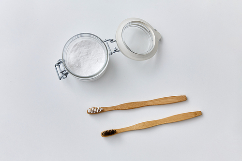 dental care, sustainability and eco living concept - washing soda in glass jar and wooden toothbrushes on white background