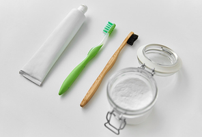 dental care, sustainability and eco living concept - wooden and plastic toothbrush, toothpaste and washing soda in glass jar on white background
