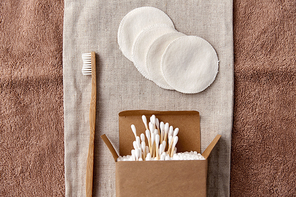 natural cosmetics, sustainability and eco living concept - wooden toothbrush, cotton pads and swabs in paper box on canvas bag and bath towel