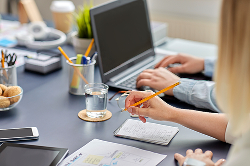 business, people and technology concept - close up of ui designer with notebook and pencil working on mobile app design at office