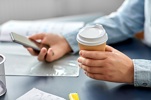 business, technology and people concept - close up of hands using smartphone and drinking takeaway coffee from paper cup at office