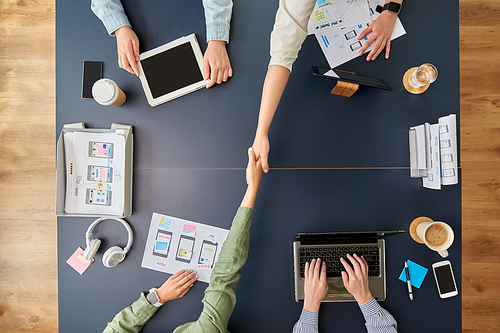 business, people and team work concept - team of startuppers with gadgets and papers makes handshake at office table