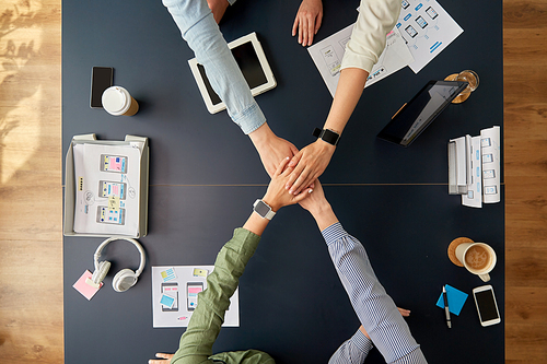 business, people and team work concept - team of startuppers with gadgets and papers stacking hands above office table