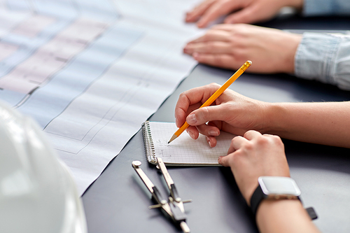 construction business, architecture and buiding concept - close up of architect with blueprint, notebook and pencil working at office