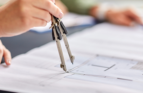 construction business, architecture and building concept - close up of architect with blueprint and drafting compass working at office