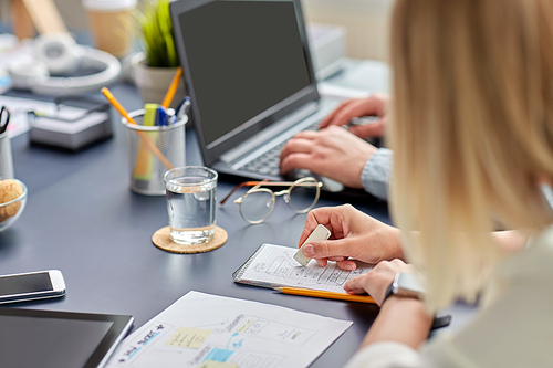 business, people and technology concept - close up of ui designer with notebook and eraser working on mobile app design at office