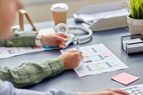 business, people and technology concept - close up of ui designer with mockups working on mobile app design at office