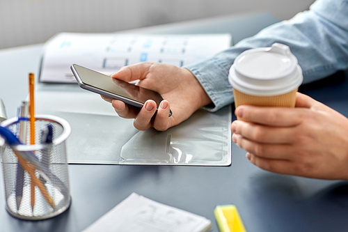 business, technology and people concept - close up of hands using smartphone and drinking takeaway coffee from paper cup at office