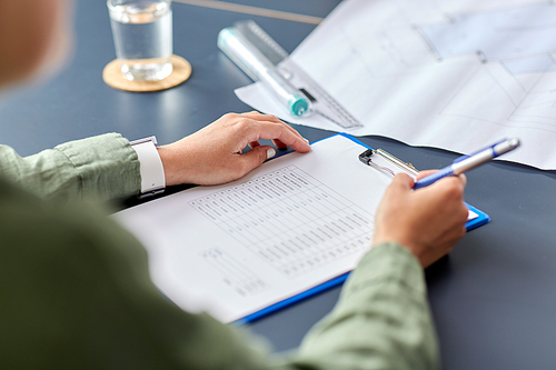 construction business, architecture and building concept - close up of architect with estimate on clipboard and blueprint pen working at office