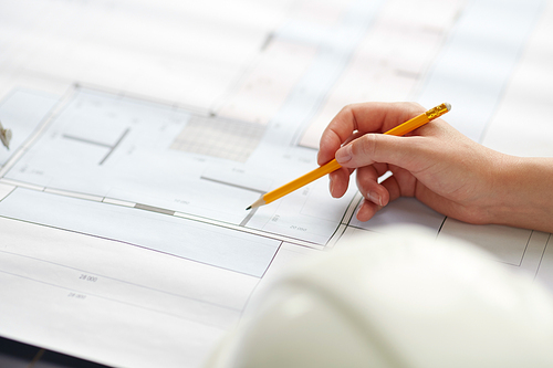 construction business, architecture and building concept - close up of architect with blueprint and pencil working at office