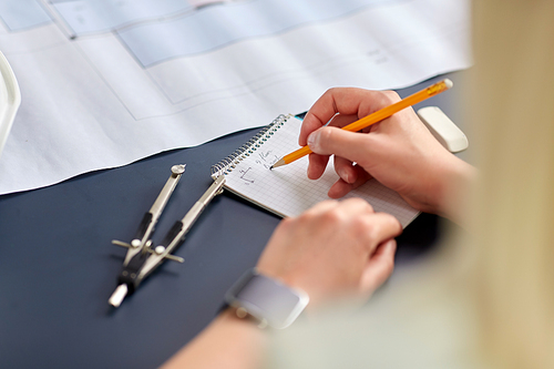 construction business, architecture and building concept - close up of architect with blueprint, notebook and pencil working at office