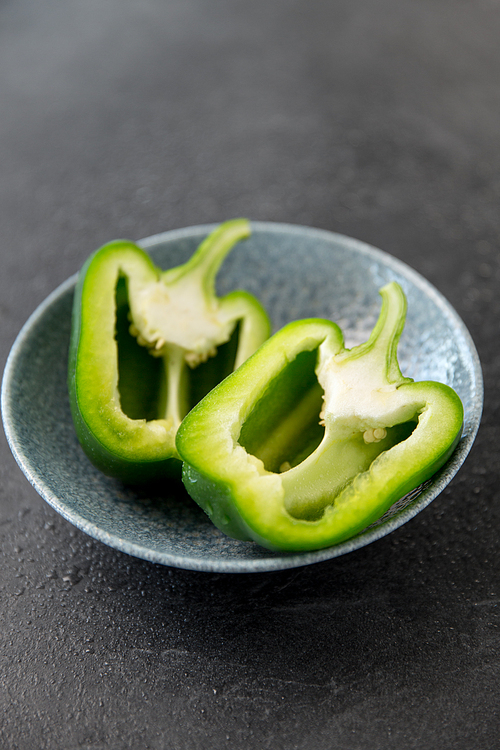 vegetable, food and culinary concept - close up of cut green pepper in bowl on slate stone background