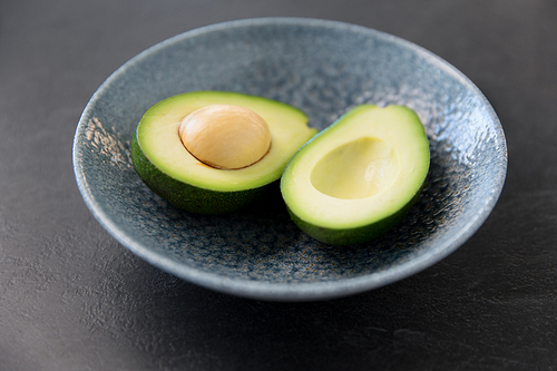 food, eating and vegetable concept - close up of cut avocado with bone in ceramic bowl on slate stone background