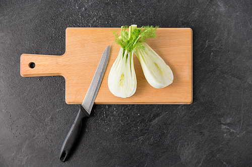 vegetable, food and culinary concept - close up of fennel and kitchen knife on wooden cutting board on slate stone background