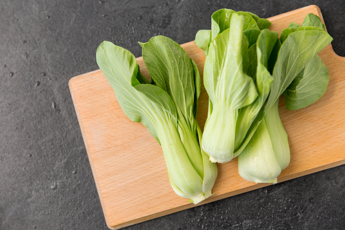 vegetable, food and culinary concept - close up of bok choy chinese cabbage on wooden cutting board on slate stone background