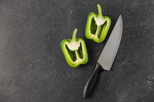 vegetable, food and culinary concept - close up of cut green pepper and kitchen knife on slate stone background