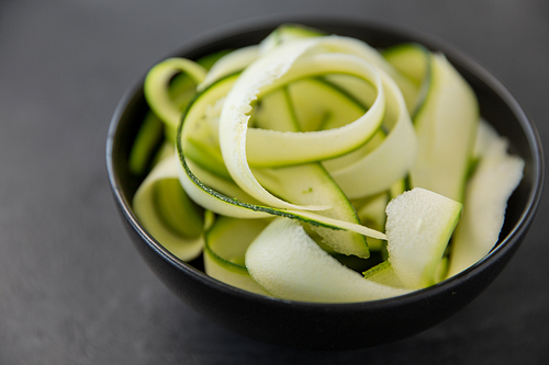 vegetable, food and culinary concept - close up of peeled or sliced zucchini in ceramic bowl on slate stone background