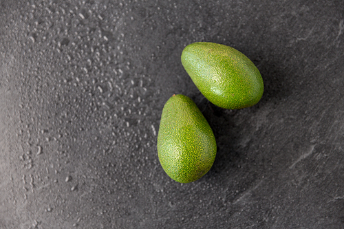 food, eating and vegetable concept - close up of two avocados on wet slate stone background