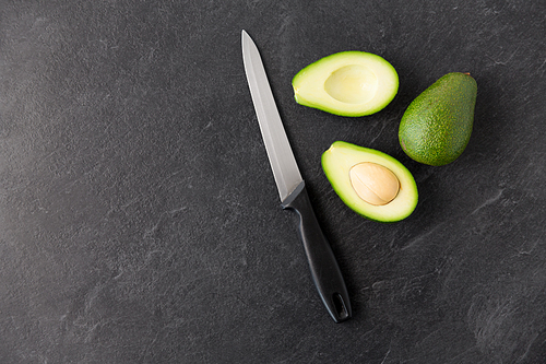 food, eating and vegetable concept - close up of cut avocados with bone and kitchen knife on slate stone background